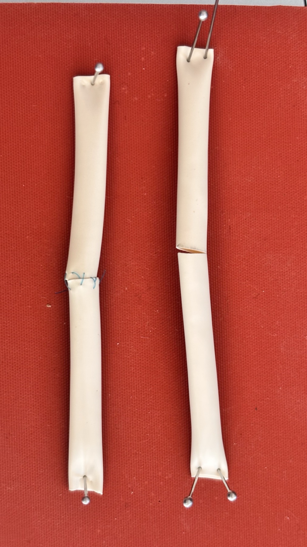 Two synthetic vessel specimens on a surgical mat, one sutured and one cut